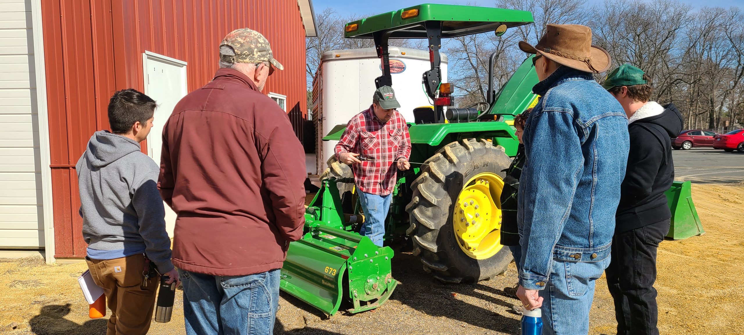 farmers gathered around a green tractor as an educator teaches them