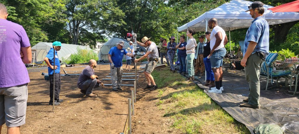 farmers installing ground posts for high tunnels with a group of other farmers looking on