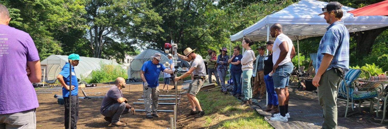 farmers installing ground posts for high tunnels with a group of other farmers looking on