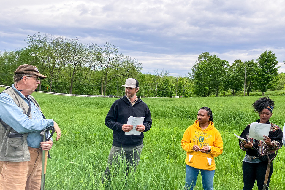 three participants of a farmers training class in a field of tall grass. 