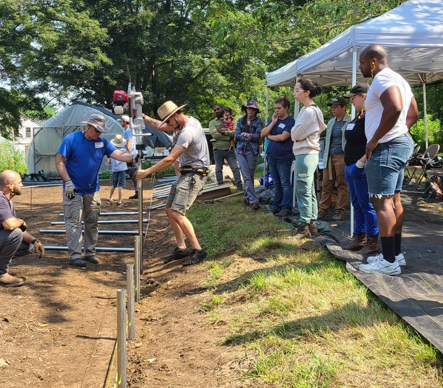 farmers installing ground posts for high tunnels with a group of other farmers looking on