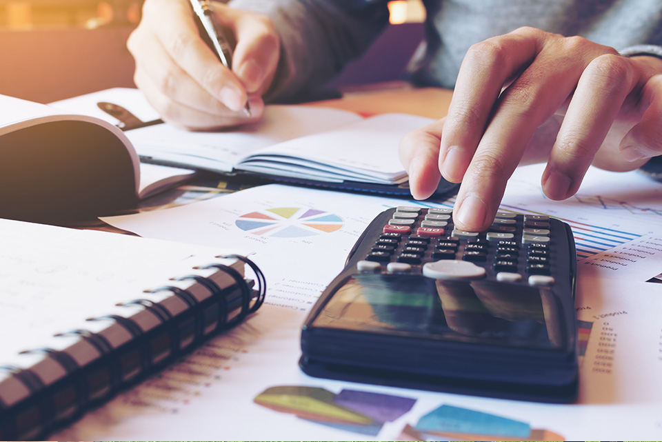 paperwork on a desk while someone uses a calculator and pen.