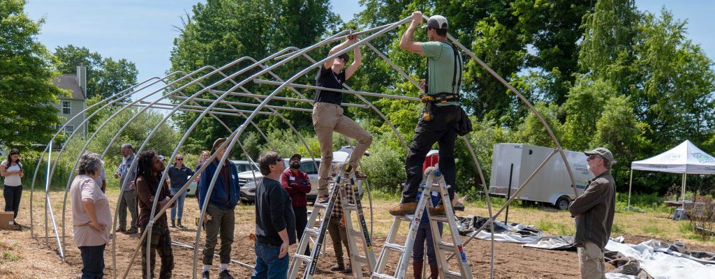 a group of people outside building a greenhouse framework.
