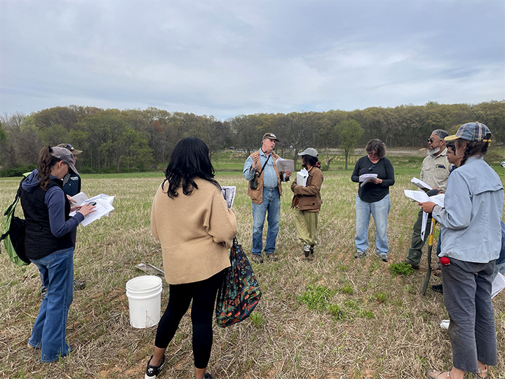 Participants at April's Farmland Seeking Skill Share review soil maps all standing in a field.